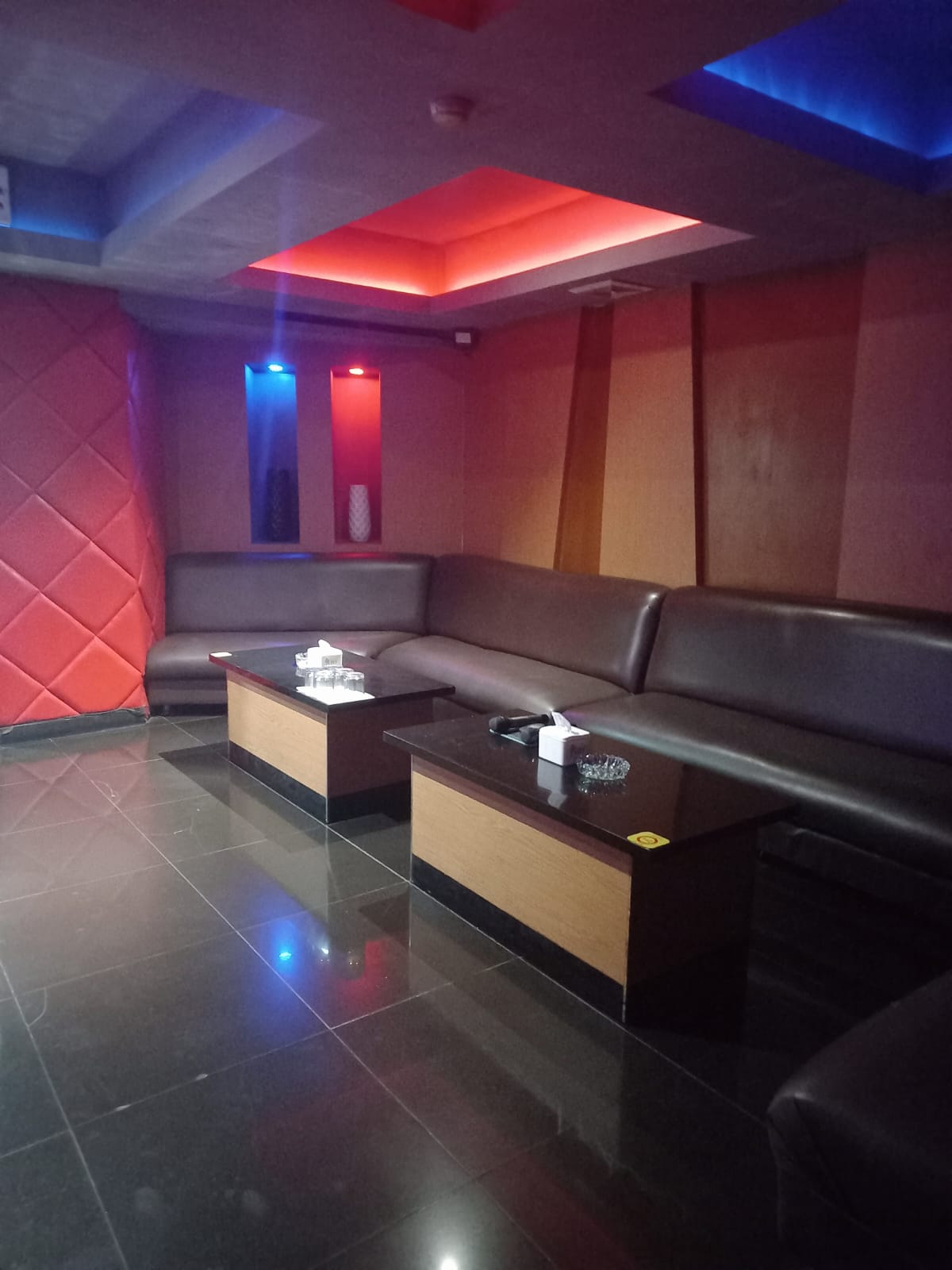 Ruang lounge dengan sofa sudut cokelat dan lampu plafon merah-biru