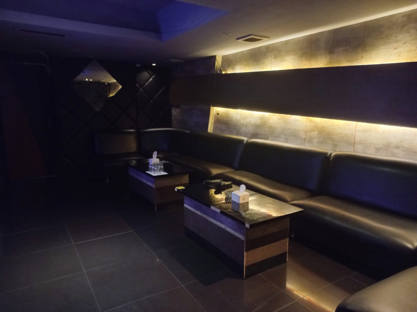 Ruang dengan sofa kulit hitam panjang dan lampu dinding hangat keemasan